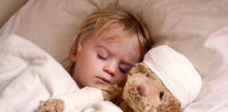 A boy is in bed with his teddy bear. The bear has a bandage around its head.