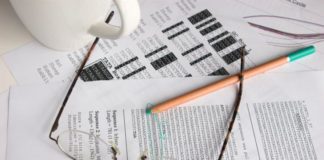 There are a few sheets of paper with code on them, a pair of glasses and a green pen. There is also a white mug.