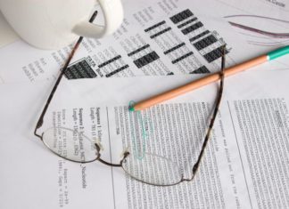 There are a few sheets of paper with code on them, a pair of glasses and a green pen. There is also a white mug.