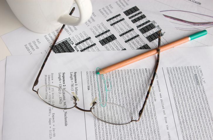 There are a few sheets of paper with code on them, a pair of glasses and a green pen. There is also a white mug.