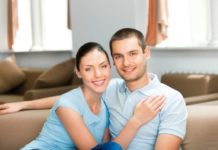 A smiling couple sit in a conservative pose.