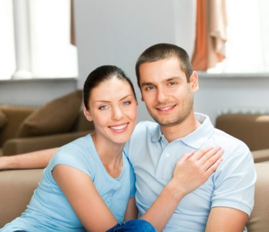 A smiling couple sit in a conservative pose.