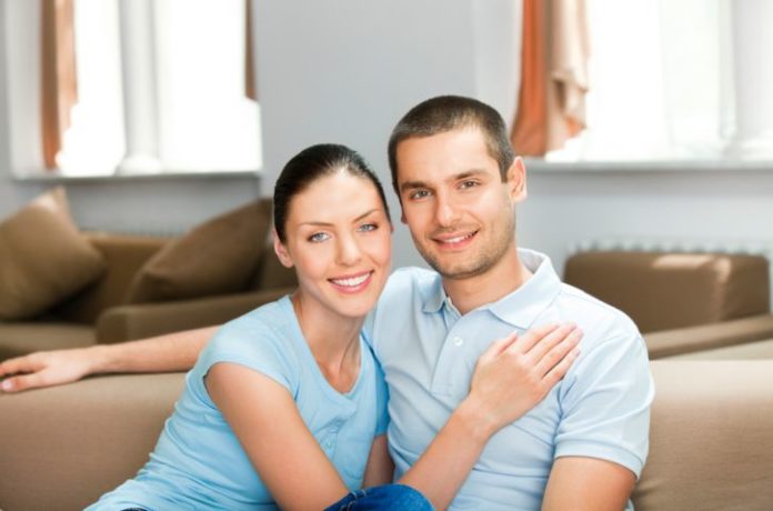 A smiling couple sit in a conservative pose.