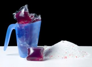 Various kinds of laundry detergent on a white counter with a black backdrop.