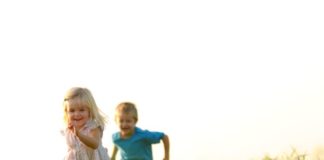 Boy and girl running and playing on grassy hill.