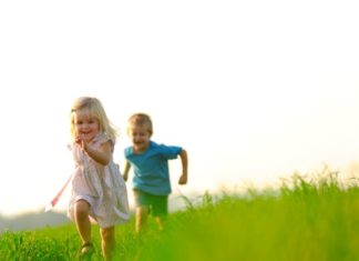 Boy and girl running and playing on grassy hill.
