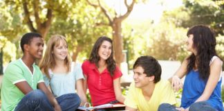 An eclectic and picture perfect group of school kids hang out on the lawn in front of a pile of books.