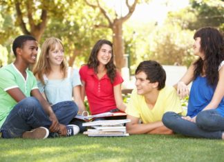 An eclectic and picture perfect group of school kids hang out on the lawn in front of a pile of books.