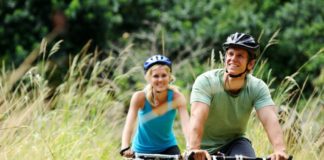 A couple, dressed in mountain biking gear, bike through tall grass. They look very happy.