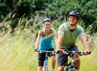 A couple, dressed in mountain biking gear, bike through tall grass. They look very happy.