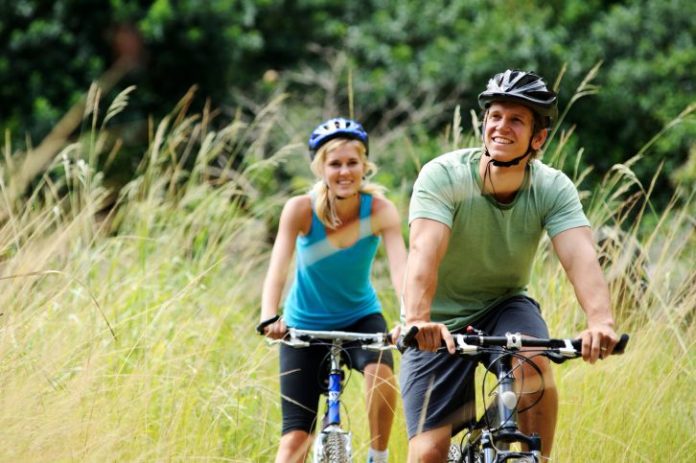 A couple, dressed in mountain biking gear, bike through tall grass. They look very happy.