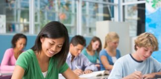 A group of teens sit in class, attentively doing their work.