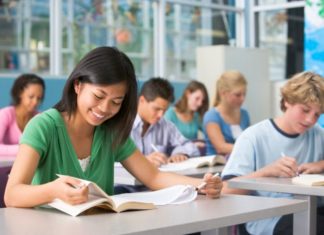 A group of teens sit in class, attentively doing their work.