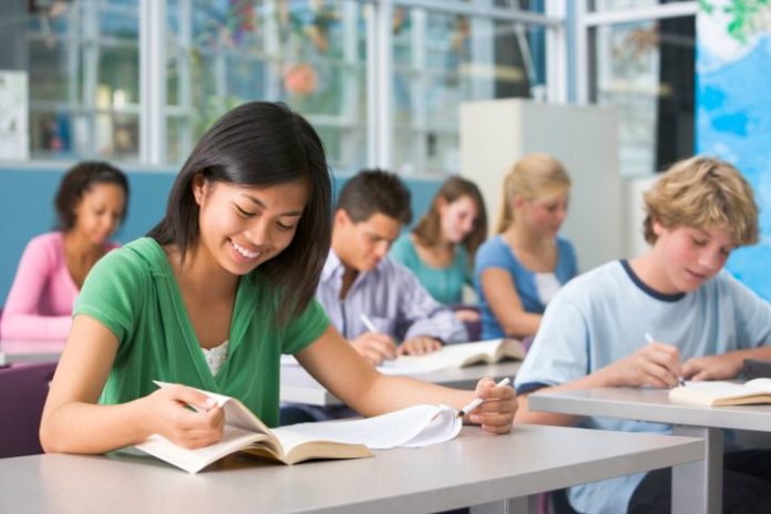 A group of teens sit in class, attentively doing their work.