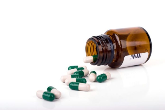 A brown glass bottle of pills tipped on its side with green and white capsules pouring out.