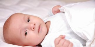 A baby wrapped in white in bed.