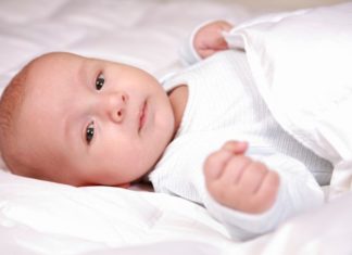 A baby wrapped in white in bed.