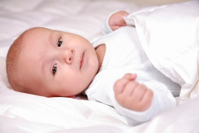 A baby wrapped in white in bed.