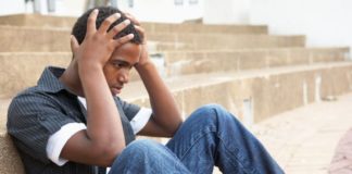 Teen boy sits on ground with his hands to his head.