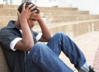 Teen boy sits on ground with his hands to his head.
