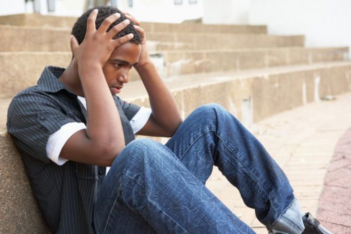 Teen boy sits on ground with his hands to his head.