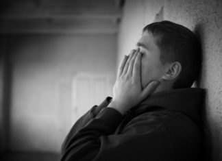 Teenager leans against wall, covering face with hands.