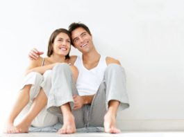 Couple in pajamas, leaning against the wall, smiling and thinking.