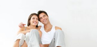 Couple in pajamas, leaning against the wall, smiling and thinking.