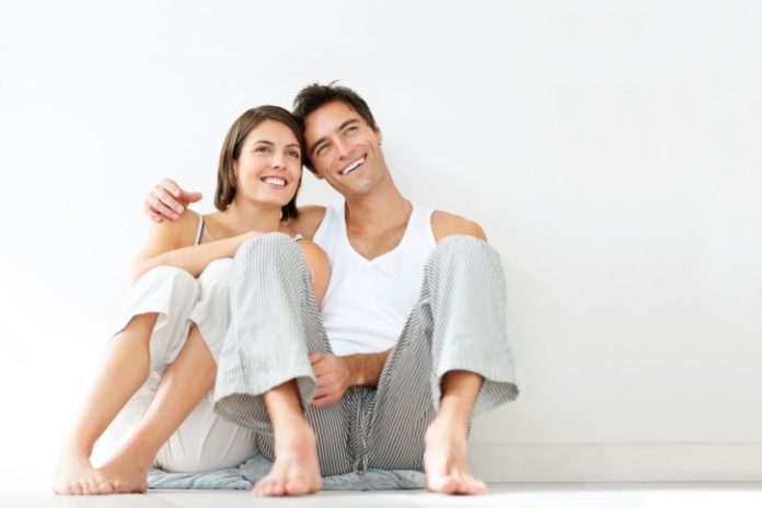 Couple in pajamas, leaning against the wall, smiling and thinking.