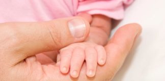 A very small baby's hand sits in the hand of her father.
