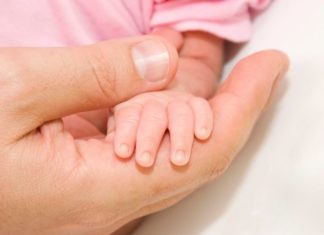 A very small baby's hand sits in the hand of her father.