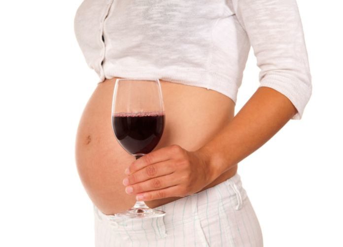 Pregnant woman holds a glass of wine near her belly.
