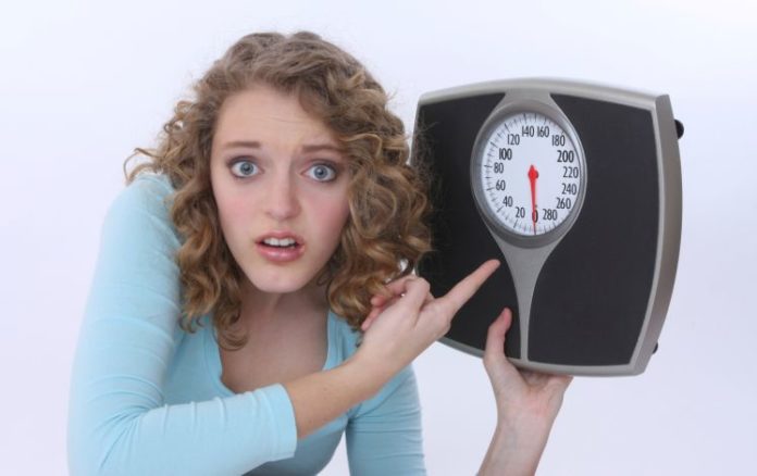 Girl holds a scale and points to it.