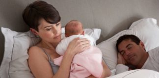 Man sleeps while unhappy looking mother holds baby.
