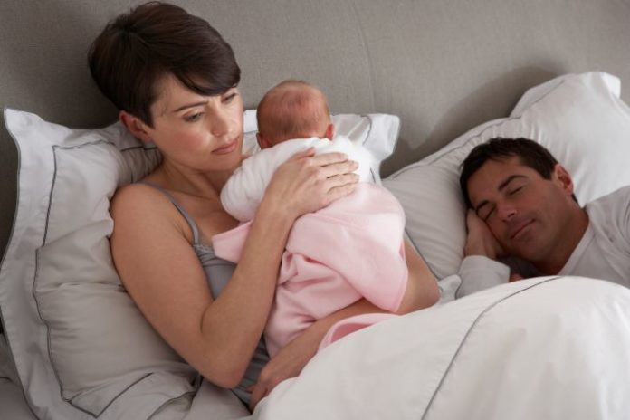 Man sleeps while unhappy looking mother holds baby.