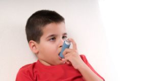 Boy in bed takes his inhaler.