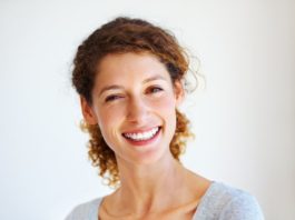 A smiling young woman with her hair in a ponytail. The light shines through her hair, catching the amber hue.