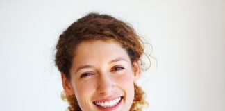 A smiling young woman with her hair in a ponytail. The light shines through her hair, catching the amber hue.