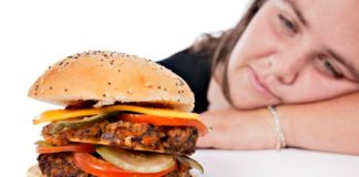 Large burger with woman in the background.