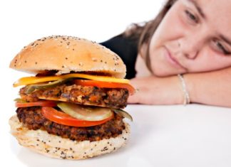 Large burger with woman in the background.