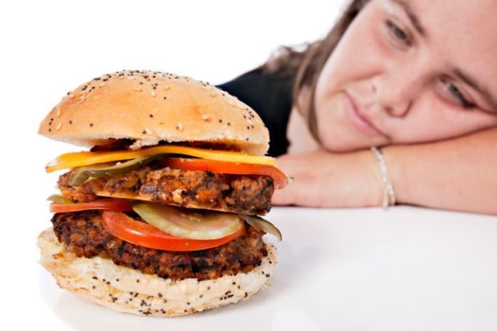 Large burger with woman in the background.