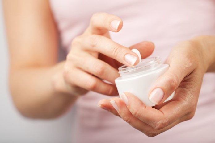 Woman holds a small jar of lotion.