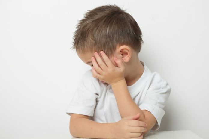 Small boy hides the side of his face with one hand.