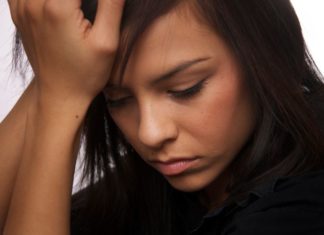 Depressed teen girl holds her head in her hands.
