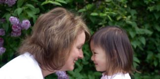 A woman and a girl face one another and smile.