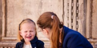 A woman a little girl sit on the steps of a building. The little girl is crying.