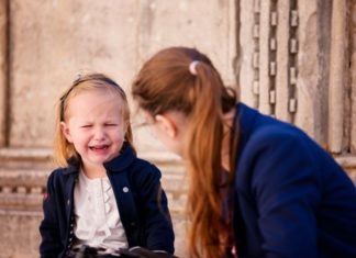 A woman a little girl sit on the steps of a building. The little girl is crying.