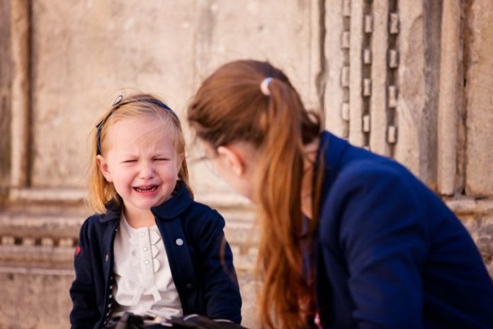 A woman a little girl sit on the steps of a building. The little girl is crying.