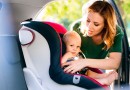 Young mother putting baby boy in the car seat.