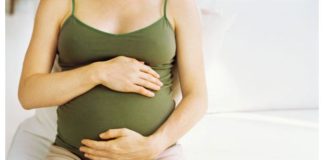 Woman sits on bed, holding pregnant belly.